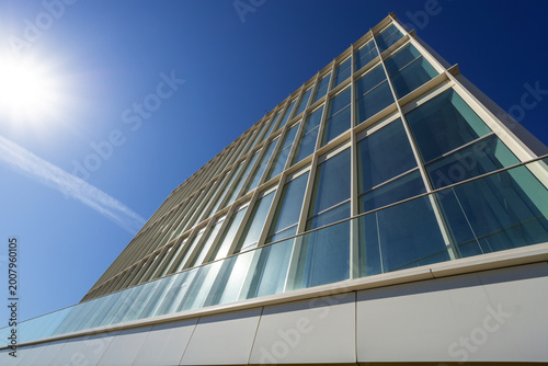 Bild auf Leinwand A tall office building with many glass windows stands under the bright sun