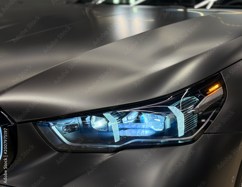 Obraz premium Front BI-LED headlight on a black matte car. Matte black premium car LED headlights close-up. Modern sport car headlight. BI-LED headlights of a modern and expensive black car, hood and radiator. 
