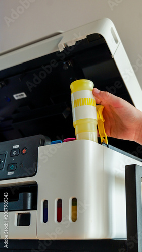 Schilderij op canvas Person refilling a printer with yellow ink cartridge, close-up view