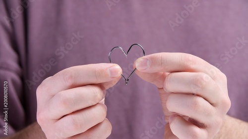 Foto Person holding two sharp fishing hooks, manipulating them to form the shape of a
