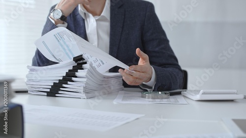 Tableau sur toile Business person analyzing financial documents with a magnifying glass, conducting an audit, reviewing reports, and investigating data on an office desk at work