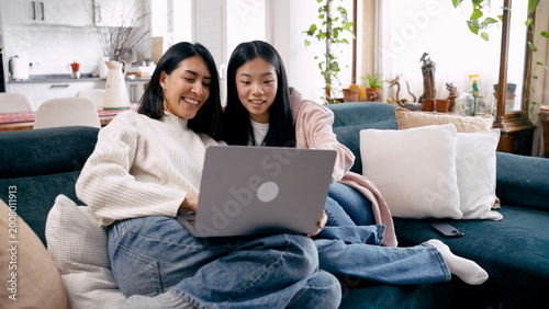 Fotografija Asian mother and teenage daughter enjoying leisure time at home, watching conten