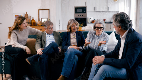 Senior friends gathering for a lively conversation, sharing moments, and enjoying togetherness on a comfortable sofa in a home setting