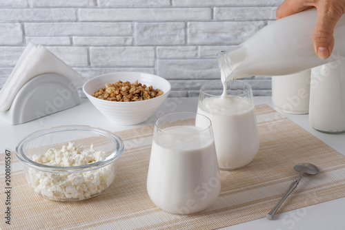 Pouring homemade kefir, buttermilk or yogurt with probiotics. Yogurt flowing from glass bottle on light background. Probiotic cold fermented dairy drink. Trendy food and drink