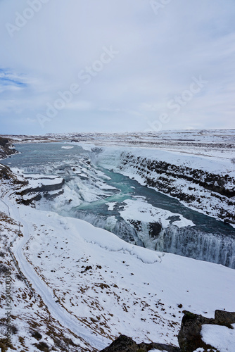 Snow-Covered Waterfall and Turquoise River Cutting Through Winter Canyon Landscape in Iceland