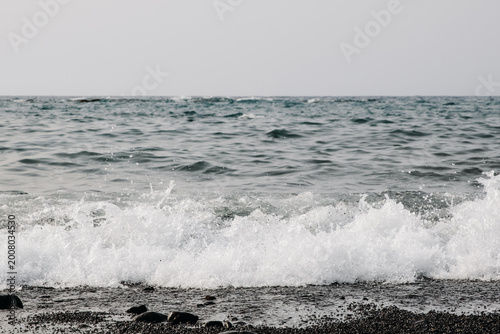 A seething wave crashes onto the shore on a black volcanic beach.