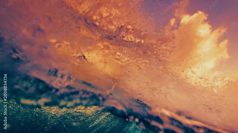 Fototapeta premium Underwater view of a breaking ocean wave with golden sunset light reflecting through the water surface and dynamic textures.