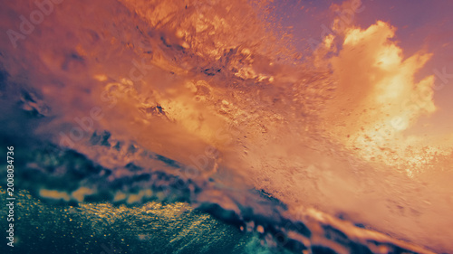 Underwater view of a breaking ocean wave with golden sunset light reflecting through the water surface and dynamic textures.