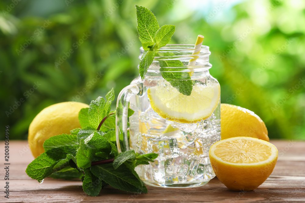 Fototapeta premium Lemon water in mason jar, mint and citrus fruits on wooden table against blurred background, closeup