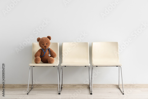 Toy bear with stethoscope on chair near light wall. Concept of pediatrics