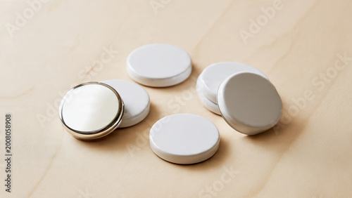White circular cosmetic disc samples with a silver-rimmed reflective mirror piece, arranged on pale wooden background, overhead shot, ideal for