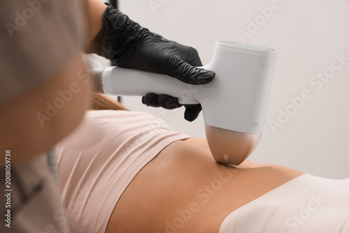 Foto Female cosmetologist performing photoepilation on client's belly in beauty salon