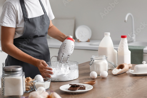 Foto Woman whipping egg albumen with mixer in kitchen