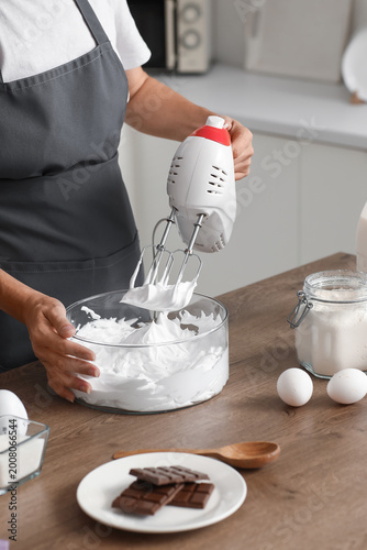 Obraz na plátne Woman whipping egg albumen with mixer in kitchen, closeup