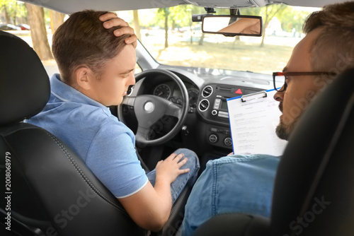 Upset young man with instructor failing driving license test in car, back view