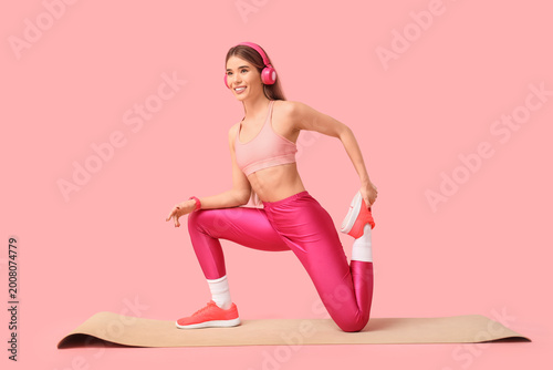 Sporty young woman with headphones practising pilates on yoga mat against pin...
