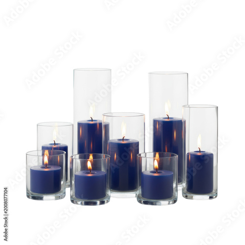 Clear glass cylinder vases of varying heights holding deep blue wax candles with warm flickering flames on a transparent surface, refined luxury atmosphere