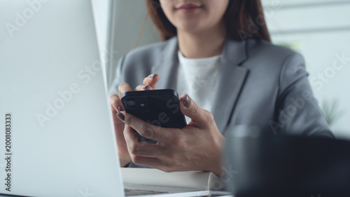 Close up of business woman using smartphone during working on laptop computer at office. 