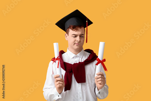 Male student in mortar board with diplomas on yellow background