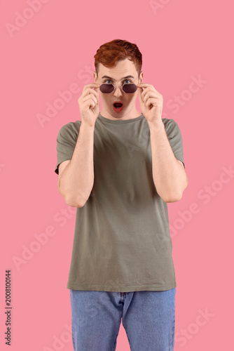 Shocked young redhead man in eyeglasses on pink background
