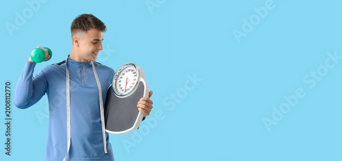 Sporty young man with scales, measuring tape and dumbbell on blue background ...