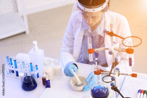 Pretty young African-American female chemist with mortar and pestle working i...