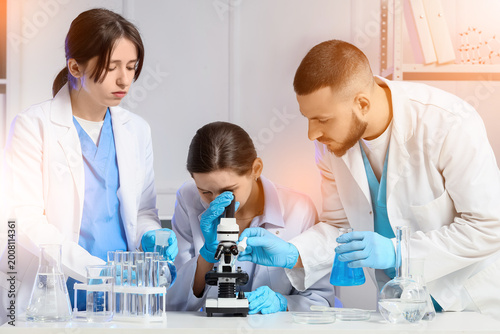 Scientists with microscope studying samples in laboratory
