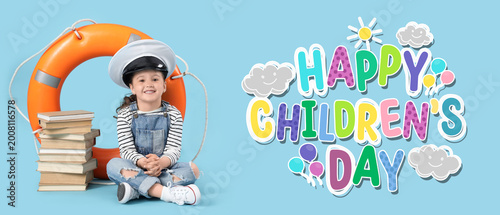 Cute little girl in pilot's hat with adventure books and ring buoy sitting on...