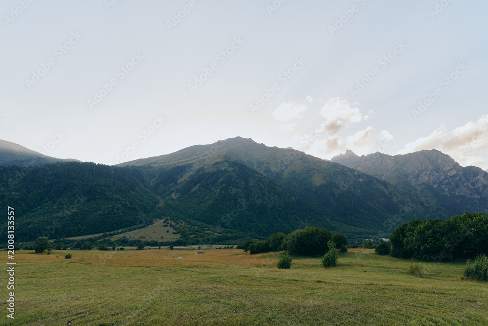 Fototapeta premium Open field with distant mountains under a clear sky, capturing vast landscape, nature, and calm. Wide horizon, gentle light, and quiet atmosphere convey solitude and freedom.