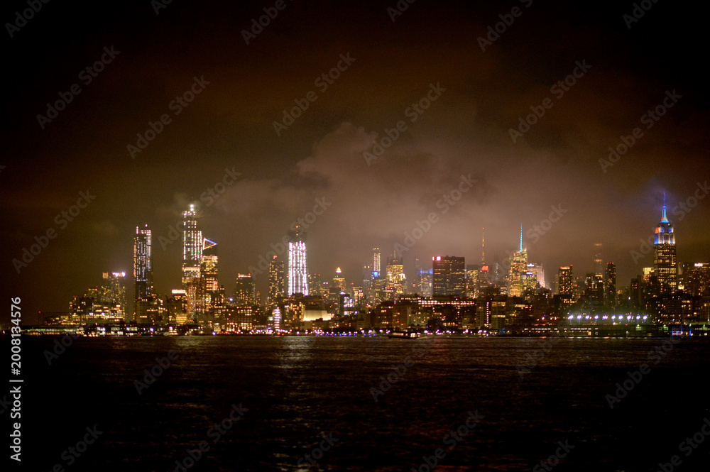 Fototapeta premium City Lights Flicker Over River. Soft Illuminated Skyline Reflects Calm Nocturnal City Atmosphere