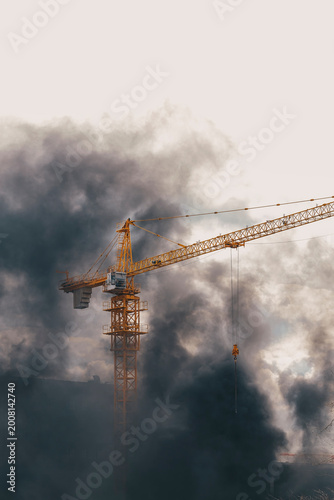 Construction crane in dense dark smoke from fire. Urban catastrophe and emergency situation idea