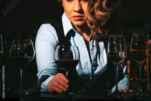 Woman expert looking at glass of red wine in dark atmosphere. Professional evaluation of vintage and variety characteristics.