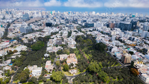 Extensive aerial landscape of the exclusive San Isidro neighborhood, perfectly blending modern glass architecture and urban development with the natural reserve of El Olivar park.