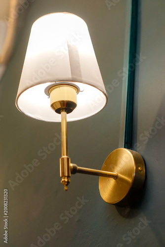 Canvas Print Elegant gold brass wall lamp with a white lampshade mounted on a dark green wall