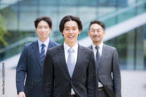 Foto 笑顔で歩くスーツで新卒採用や新人の若手ビジネスチームのポジティブ(前向き)なイメージ　転職や就活、採用などのカメラ目線の笑顔複数の横並び