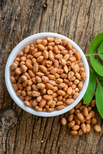 Raw peanuts in white bowl with green leaves on rustic wooden background