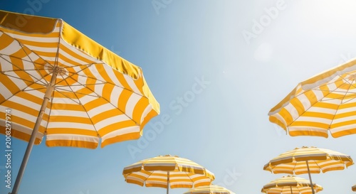 Low angle view of yellow and white striped beach umbrellas against blue sky