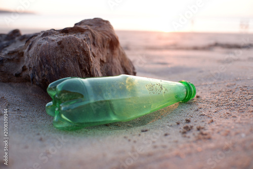 Discarded green plastic bottle littering a pristine sandy beach at sunset, a stark visual representation of plastic pollution and the urgent global environmental impact on coastal ecosystems