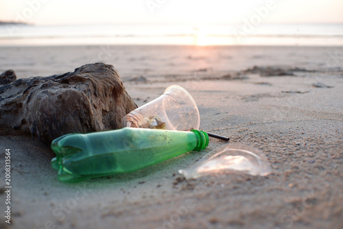 Fotografía Plastic bottle and cup litter on a beach at sunset, highlighting environmental p