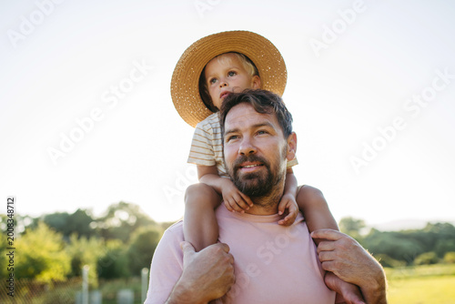 Fotografía Dad carrying little boy on shoulders during warm summer day.