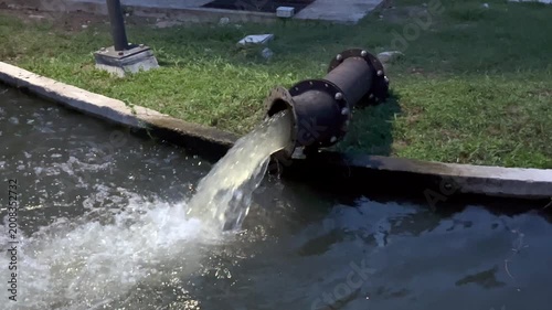 Water discharges from a large metal pipe into a canal, creating splashes and turbulence, industrial drainage system in outdoor setting, infrastructure managing flow, environmental and utility concept