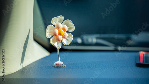 Quadro em tela small decorative plastic flower with metallic petals and yellow center shaking on dashboard during car ride highlighting vehicle interior decoration and style