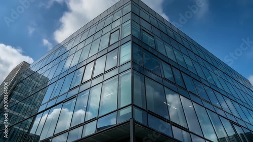 A modern glass office building stands tall under a blue sky with clouds.