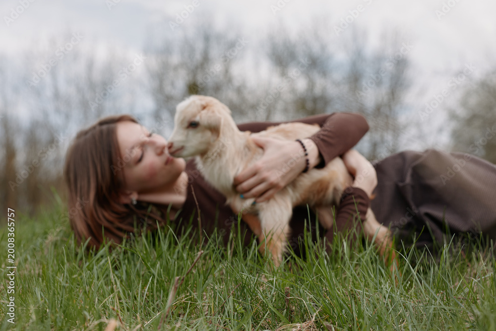 Fototapeta premium woman outdoors grass kiss affection nature countryside field lifestyle moment with goat kid in calm rural setting, tender bond between human and animal, warm light and peaceful atmosphere