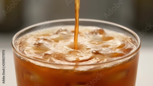 Caramel syrup pouring into iced coffee with ice cubes creating rich sweet swirl close up beverage