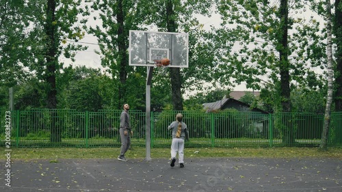 Young man practices his shooting as daughter watches eagerly at basketball court. Father with daughter enjoy day at park and playing basketball. 4K, UHD