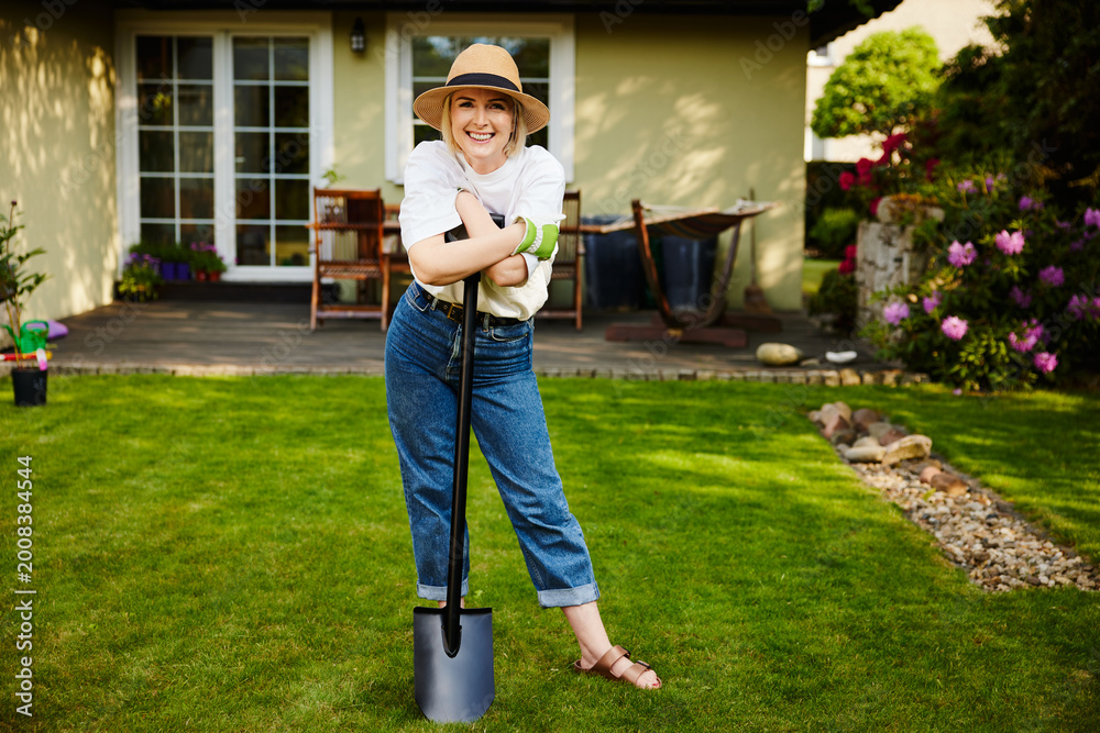 Fototapeta premium Mature woman leaning on shovel smiling in backyard garden