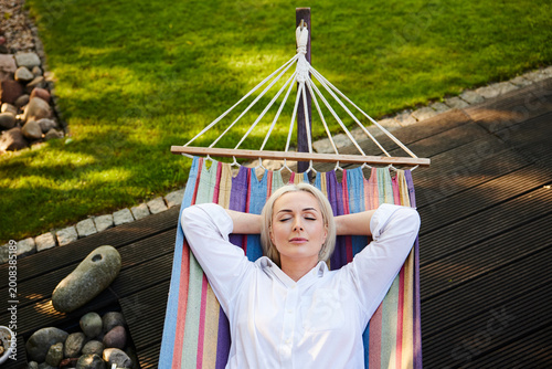 Mature woman napping in colorful hammock on garden deck