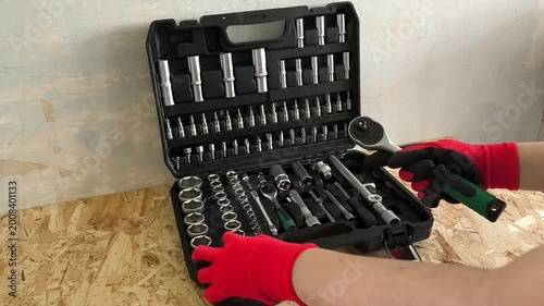 The hands of a repairman in red work gloves take a ratchet and a screwdriver attachment from a case with hand tools. Car repair shop, garage