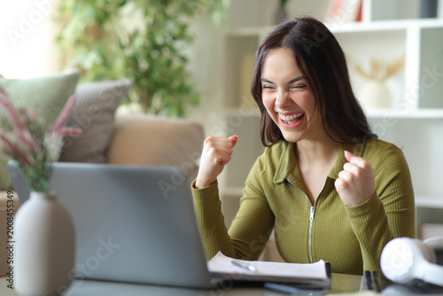 Excited student checking great news on laptop at home